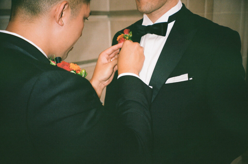 Groom putting red boutonniere on the his future husband.