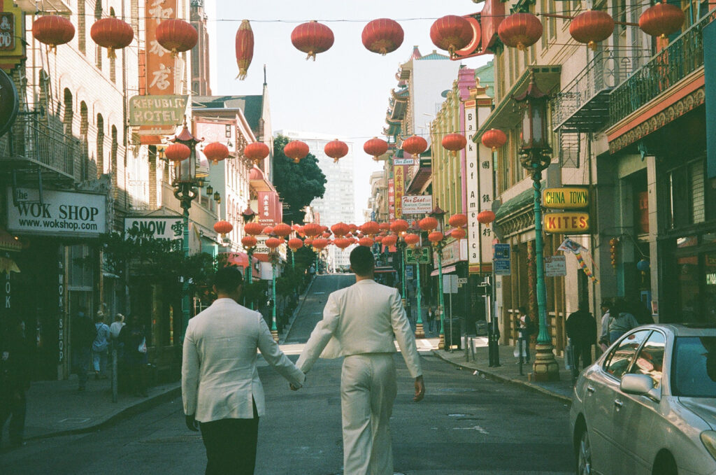 Film photo of two men holding hands through a street with hanging red Chinese lanterns.