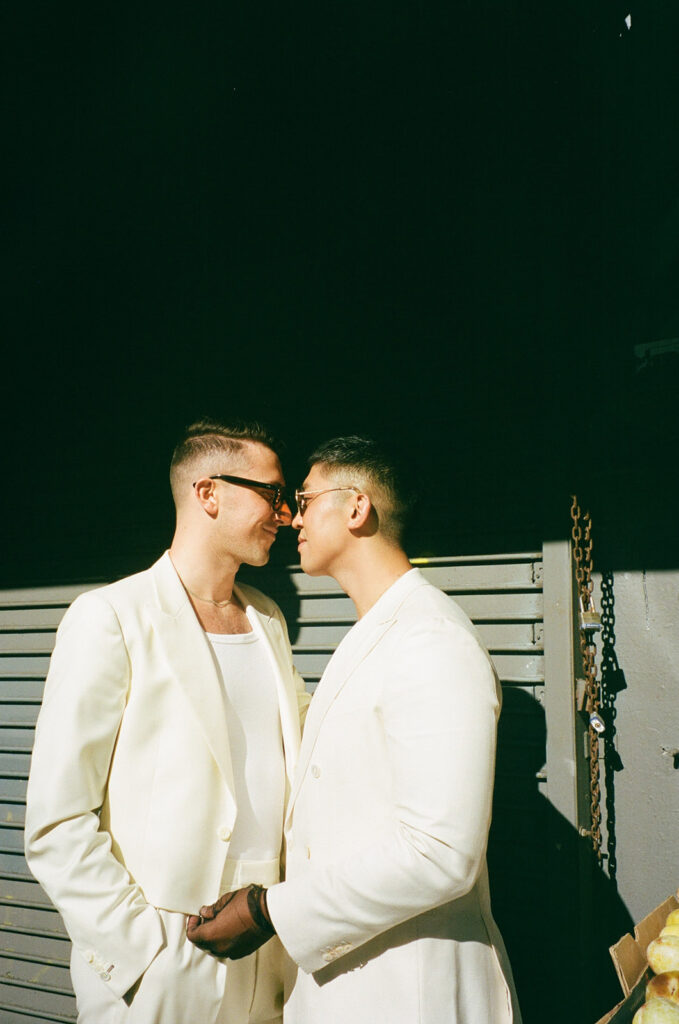 Film photo of grooms in all white touching noses.