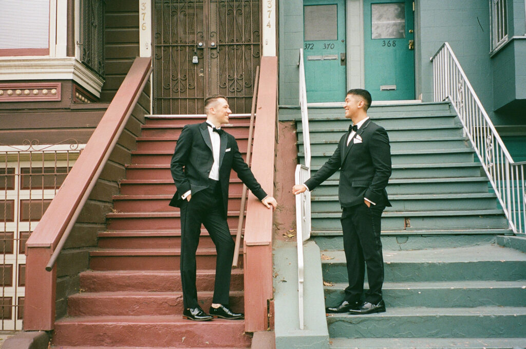 Grooms on opposite staircases, one red and the other blue, looking at each other smiling.