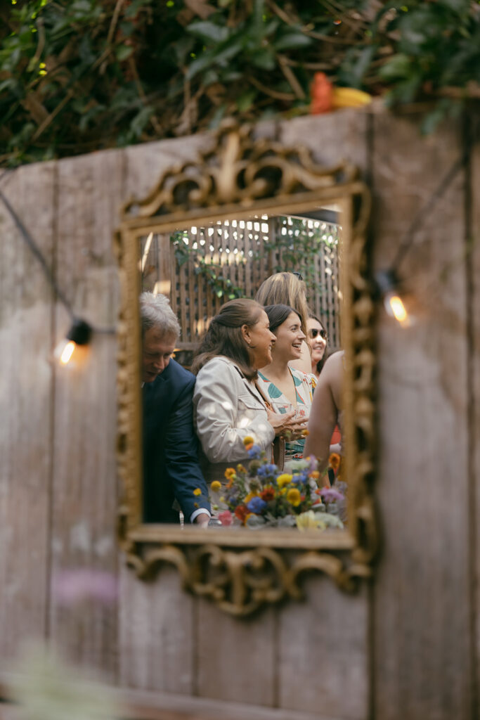 A reflection photo of wedding guests through a gold framed mirror hung in the outdoor reception.