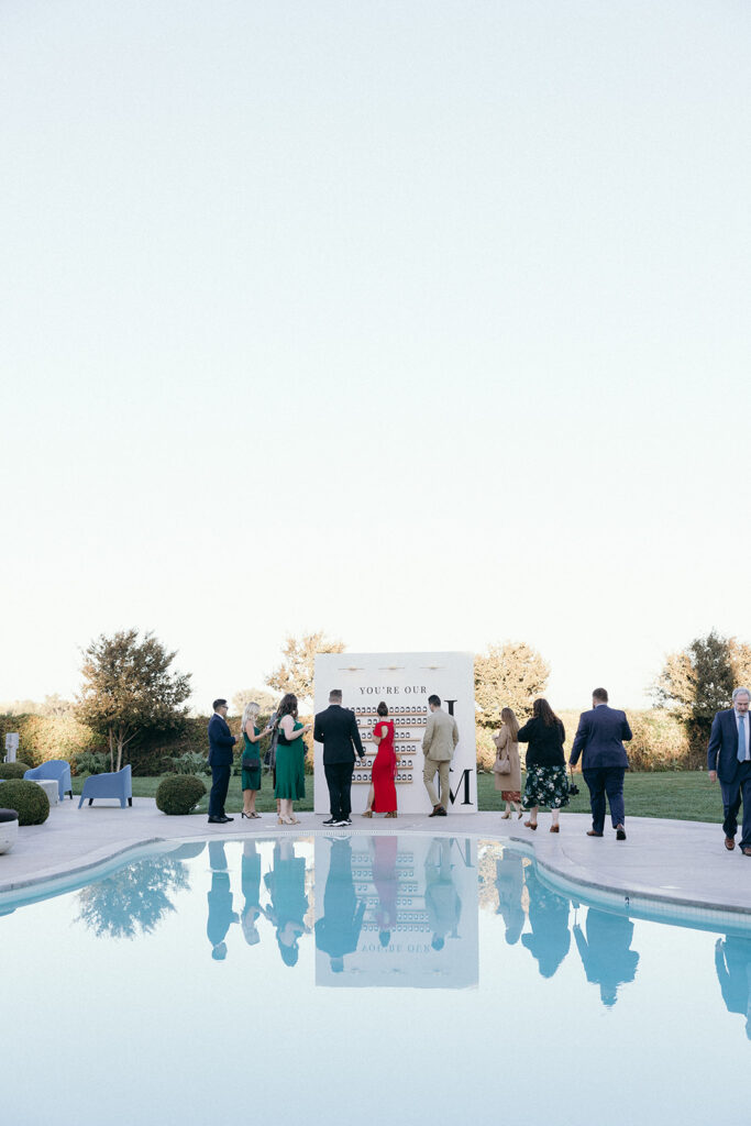 Guests looking at large white seating chart wall across the pool.