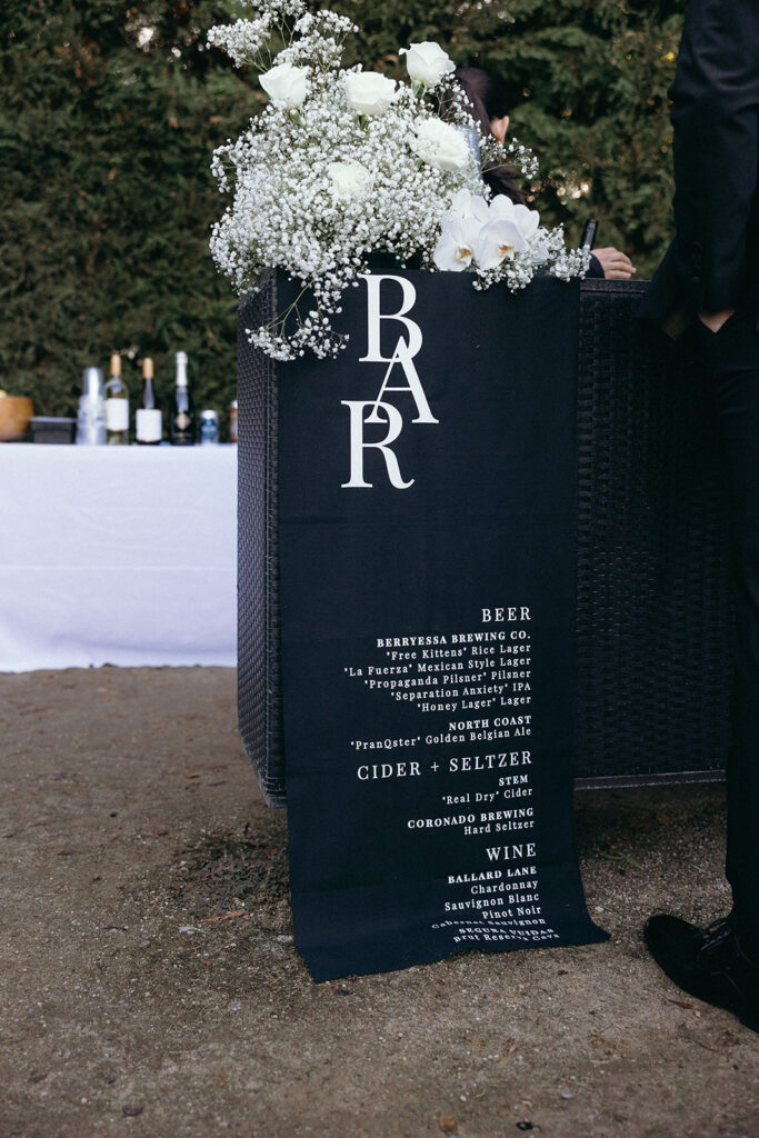 Black linen bar menu with white text and white rose and hydrangea arrangement.