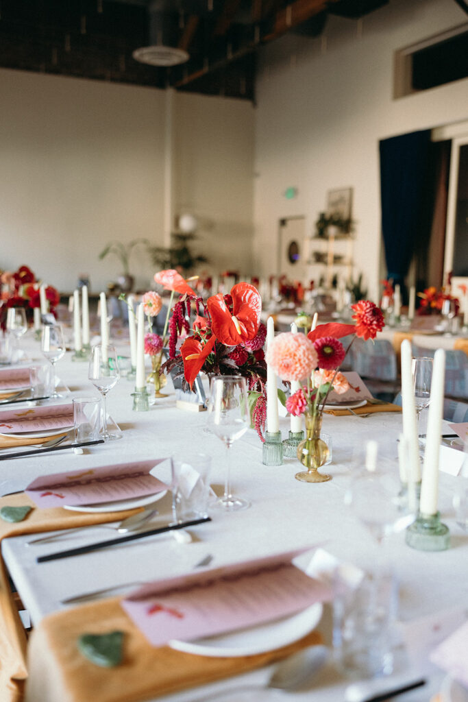 Indoor wedding tablescape with red and pink flowers and white candlesticks.