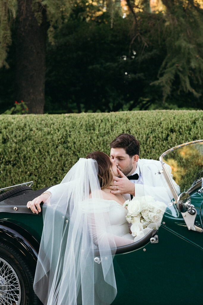 Groom softly grabbing brides face to kiss while sitting in a vintage car.