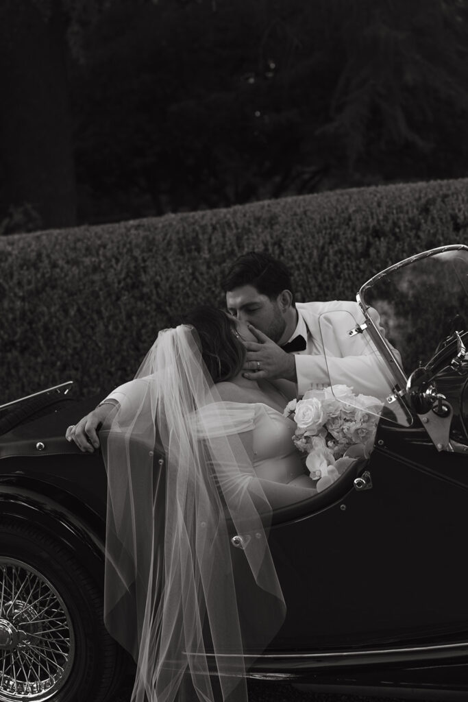 Groom softly grabbing brides face to kiss while sitting in a vintage car.
