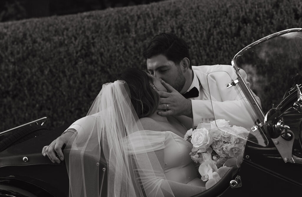 Groom softly grabbing brides face to kiss while sitting in a vintage car.