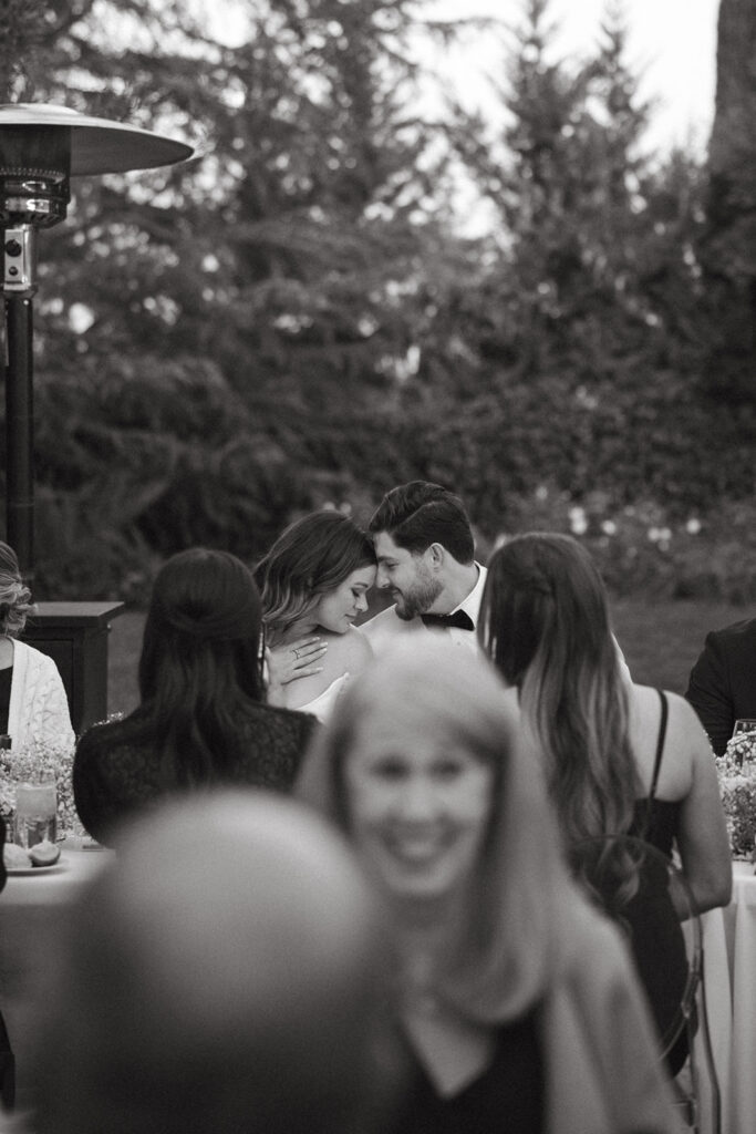 Sweet moment of the couple sitting at their reception touching foreheads while the bride has her hand on her chest.