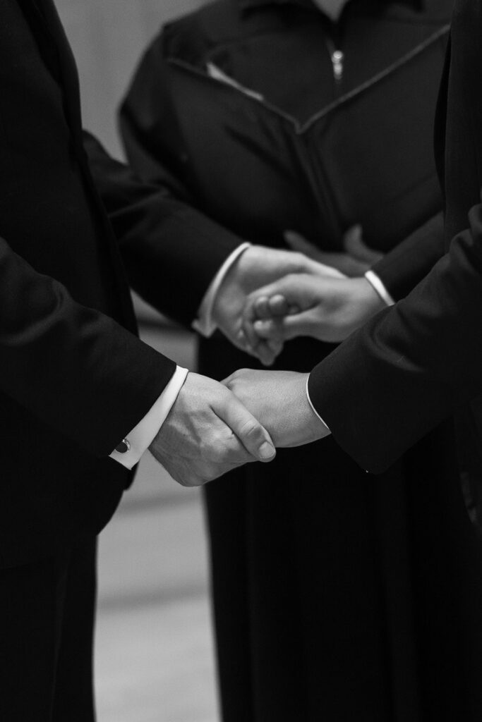 Grooms holding hands during ceremony.