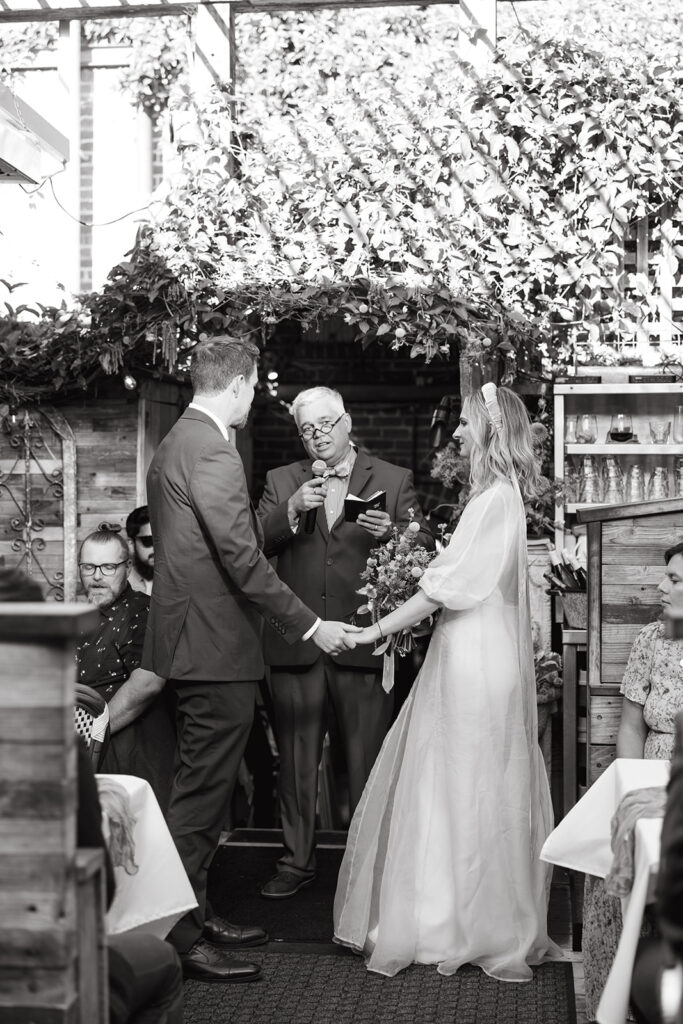 Bride and groom holding hands while listening to their officiant at the wedding ceremony.