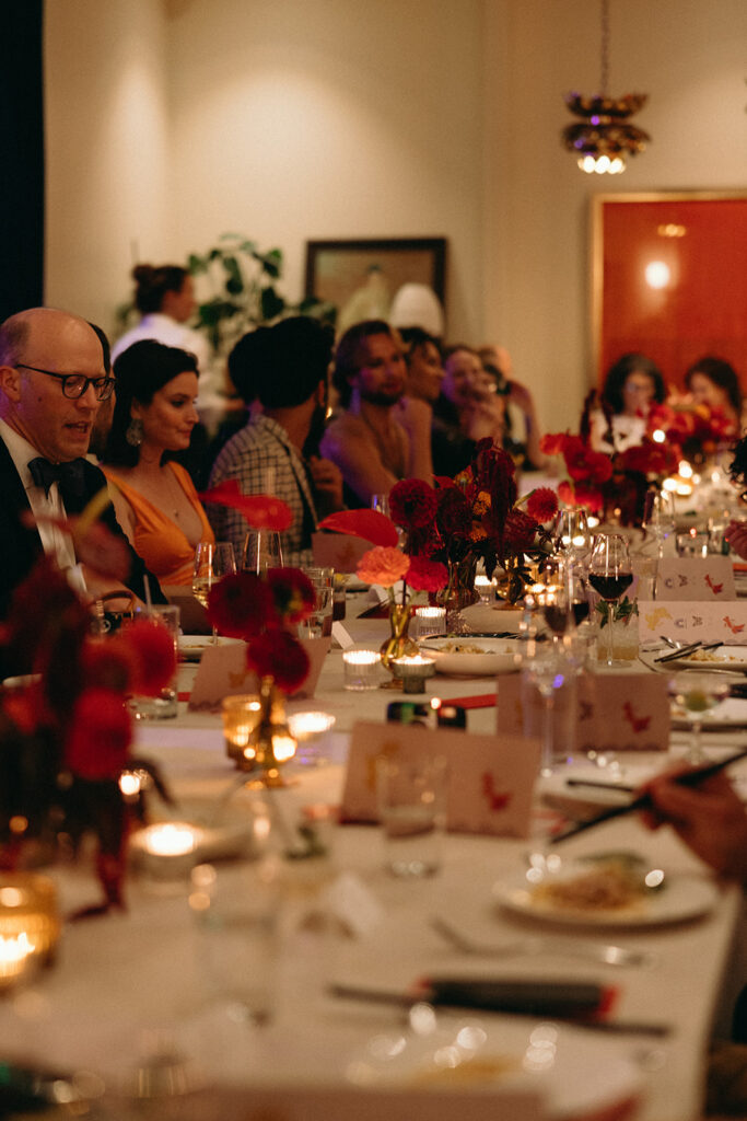 Candlelit dinner reception with red florals down the center of the table and guests enjoying themselves.