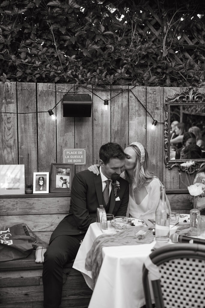 Bride kissing grooms head while sitting at their table.