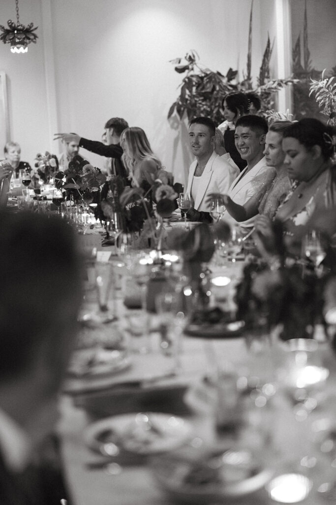 Wedding tablescape with wedding guests and grooms sitting, eating, and laughing.