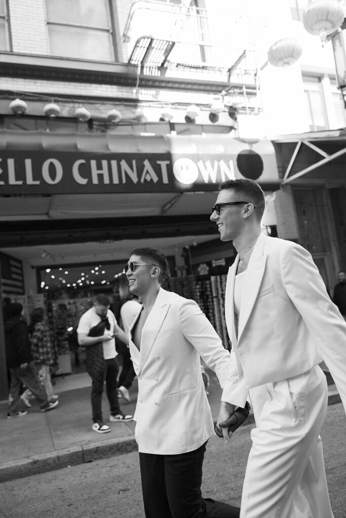 Men in all white holding hands with a Chinatown sign behind them.