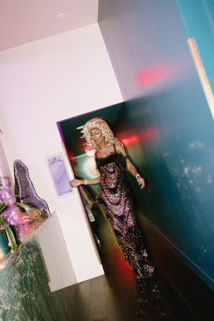 Black drag queen with blonde wig and long sparkly gown entering the wedding reception.