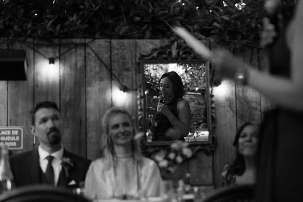 Reflection of maid of honor giving speech with view of the bride smiling at her.