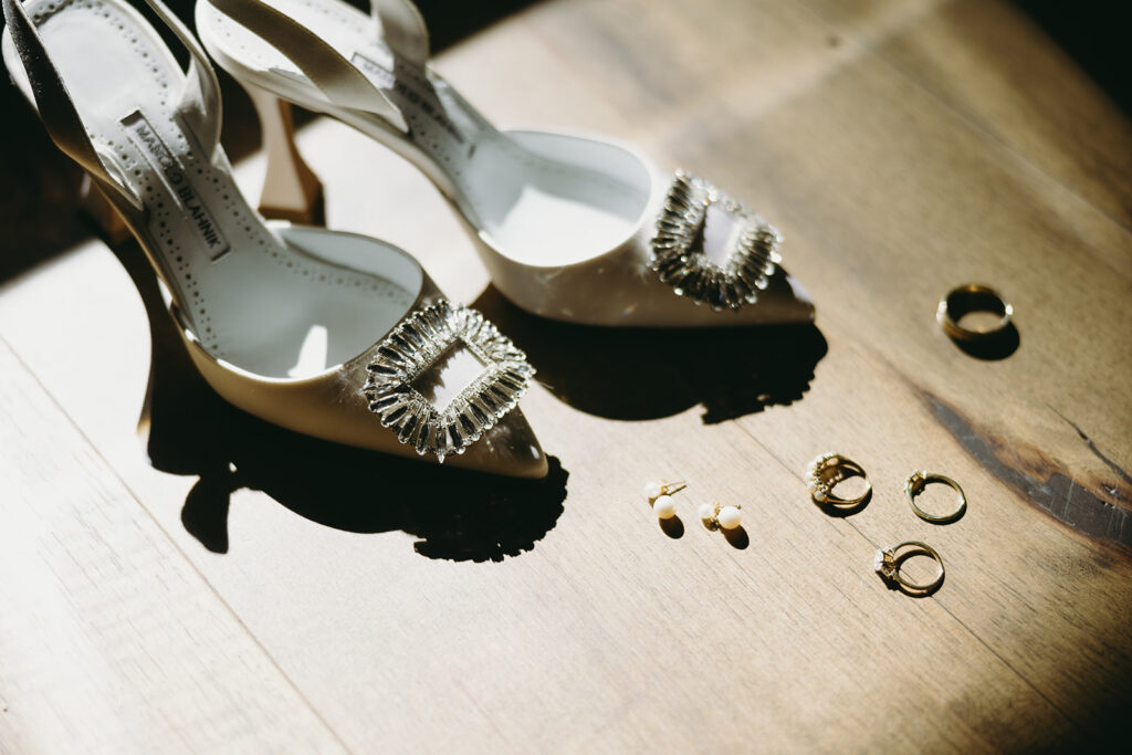 Designer white and silver bridal heels reflecting off the sunlight and pearl bridal stud earrings.