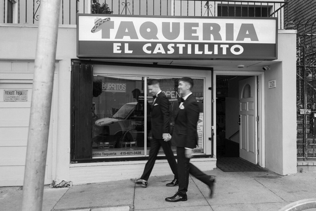 Blur of grooms walking holding hands passing a taqueria.