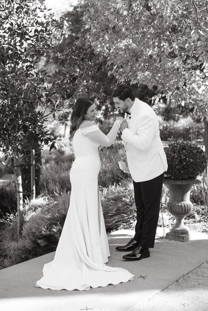 Groom holding brides handing close to his face as they giggle and look in each others eyes.