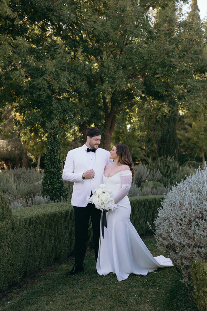 Bride and groom standing close while bride holds her white floral bouquet with black ribbons close.