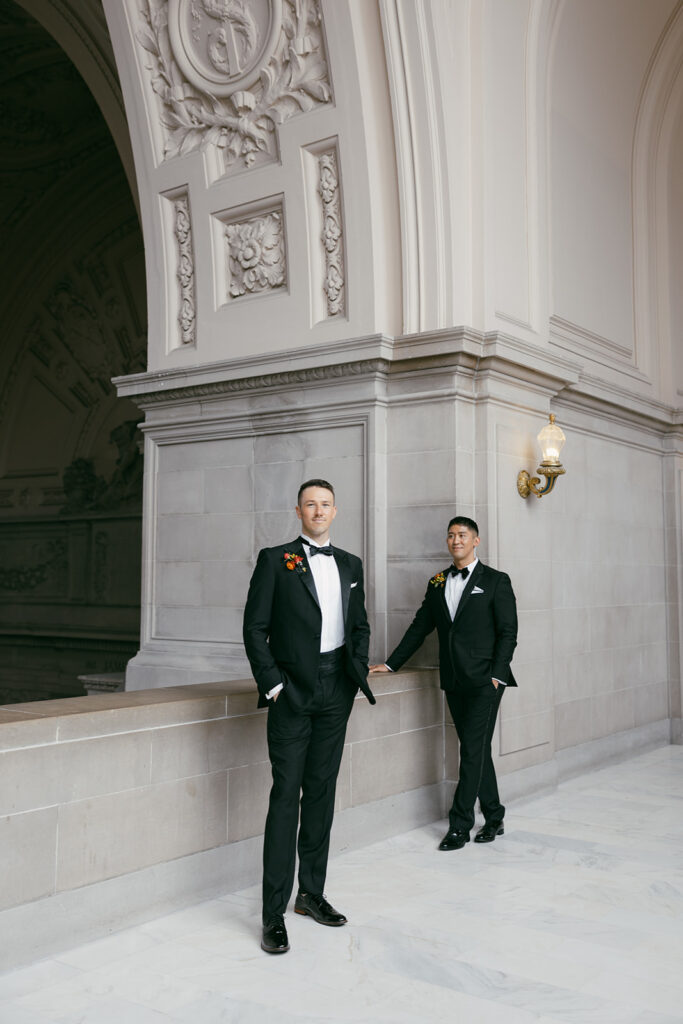 Formal gay wedding grooms posing for portraits, with one groom in the foreground and another in the background.