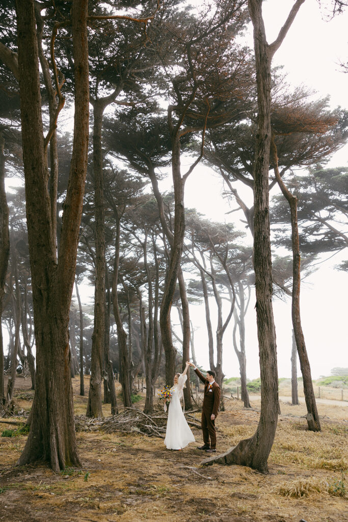 Groom spinning bride around in a circle through tall trees on the coast.