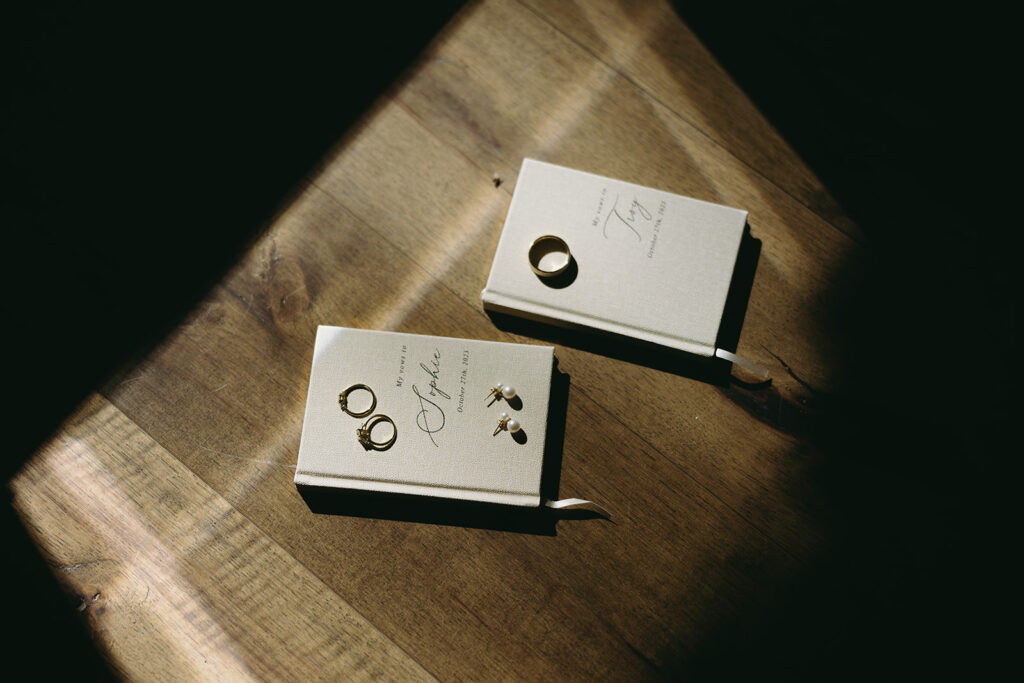 Sophie and Troy beige vow books with their wedding rings and the brides pearl earrings.