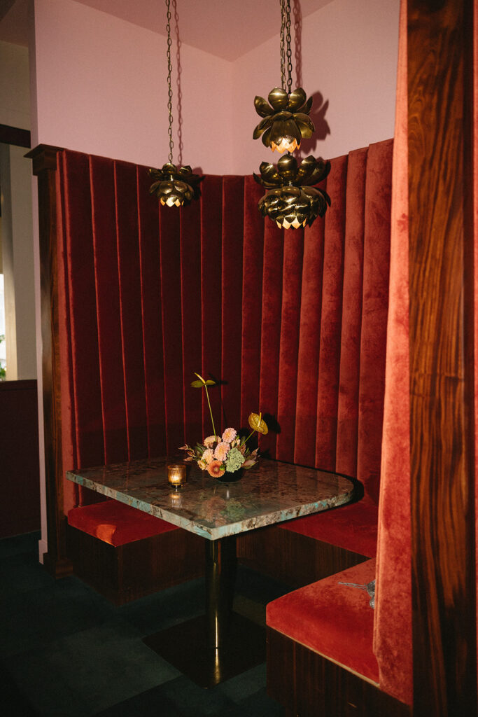 Small floral arrangement on a green and brown marble table at a red velvet booth.