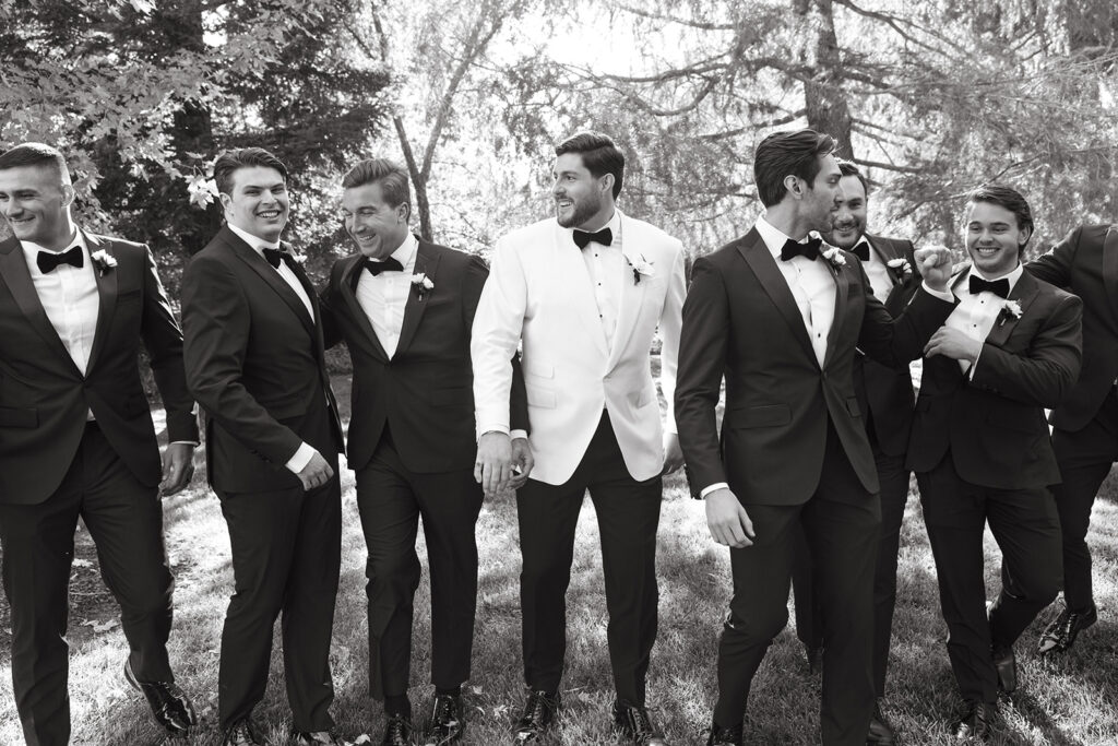 Groom in all white suit walking with his groomsmen in black suits and bow ties.