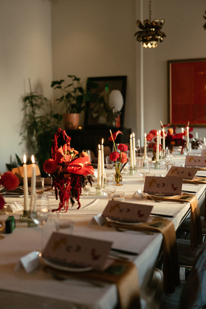 Red florals and white taper candles on a wedding tablescape in sunset golden hour glow.