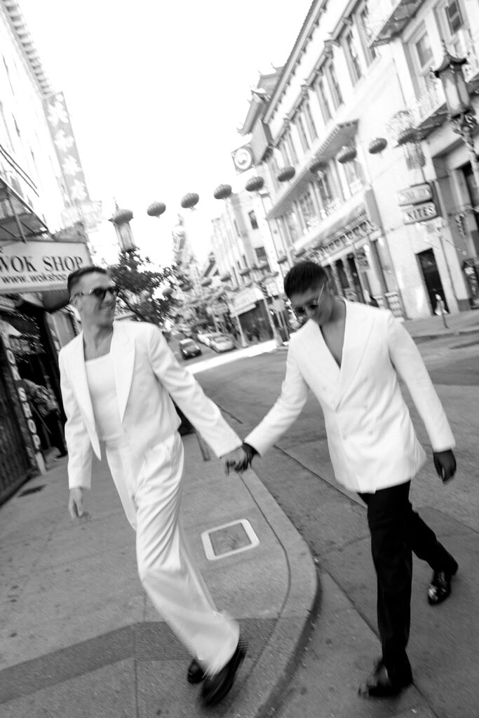 Two men, dressed in all white, holding hands walking through Chinatown in SF.