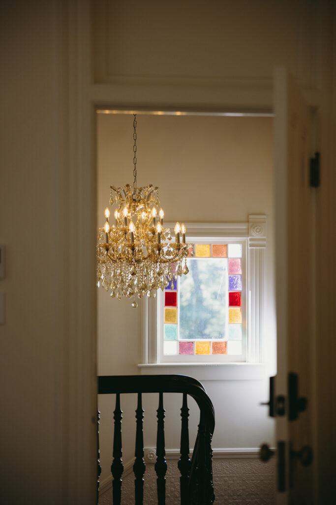 Chandelier over a staircase in front of a stained glass window where light is flowing through.