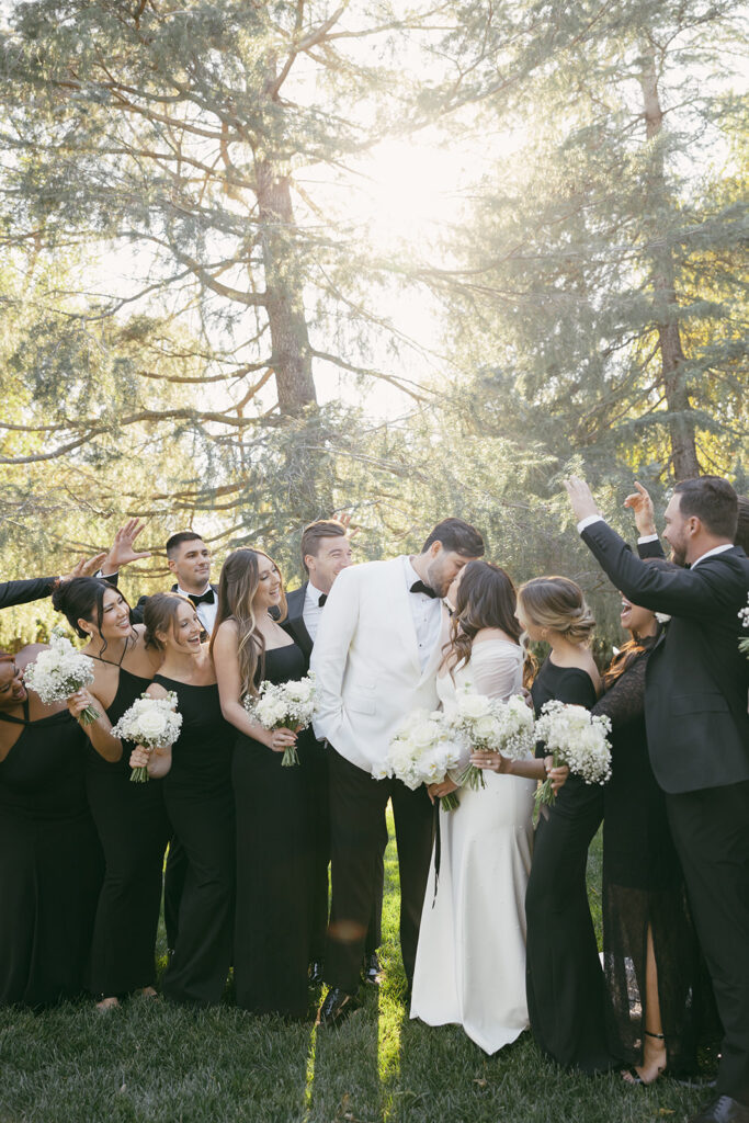 Wedding party cheering around the bride and groom as they kiss.