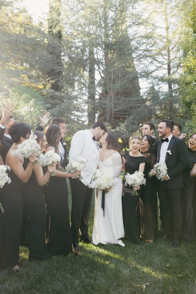 Wedding party cheering around the bride and groom as they kiss.