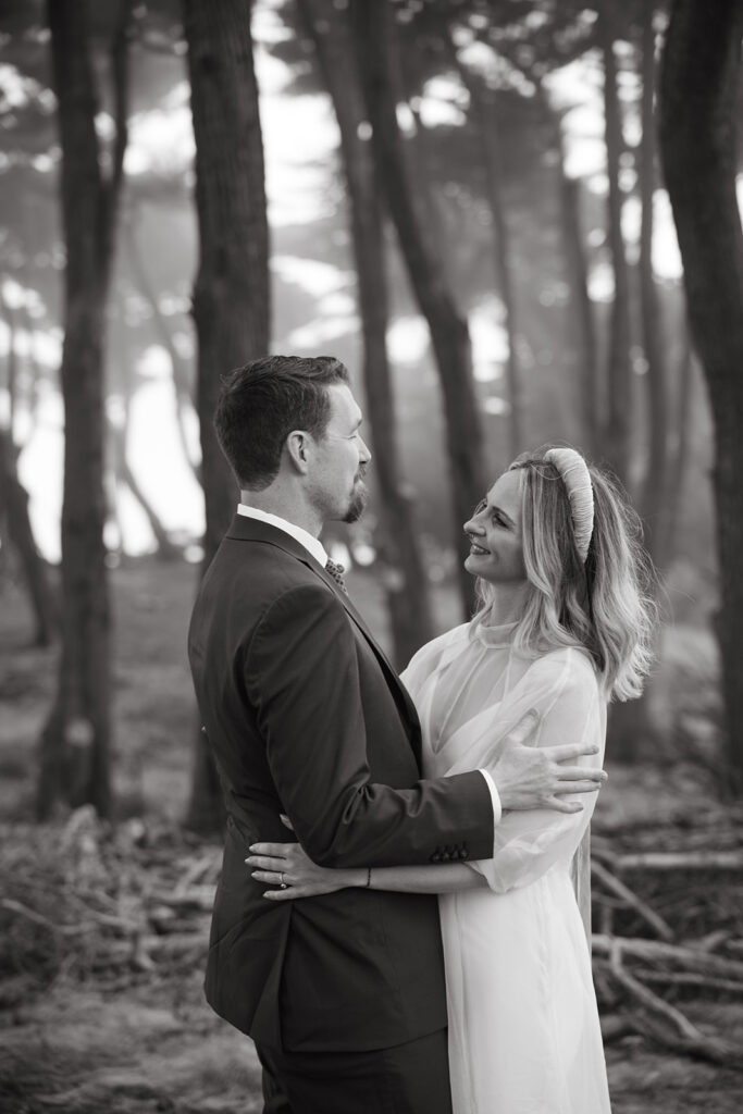 In the forest bride and groom looking into one another and smiling.
