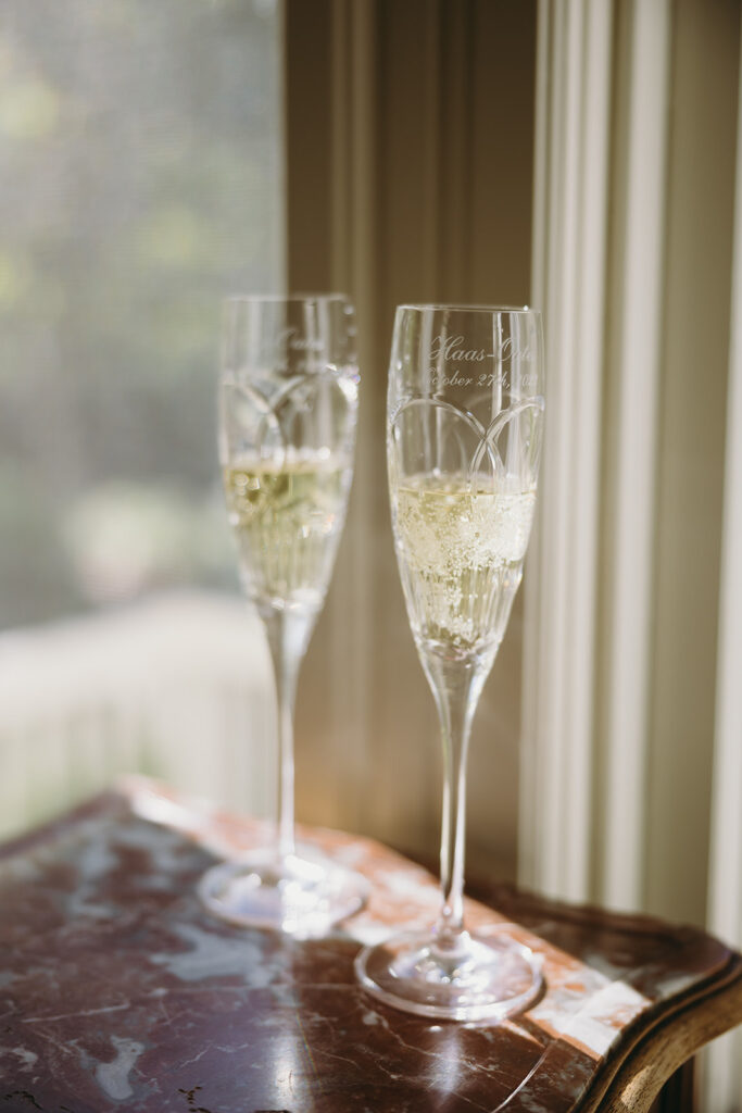 Two cursive engraved champagne flutes half filled with champagne in the sunlight.