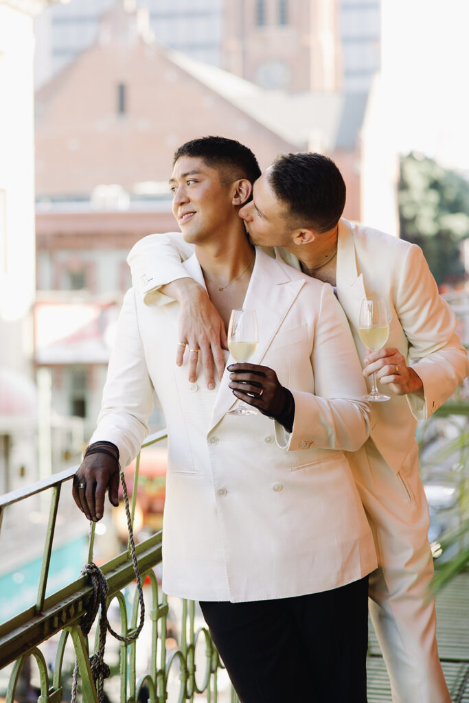 From behind, one groom kissing the other grooms neck.