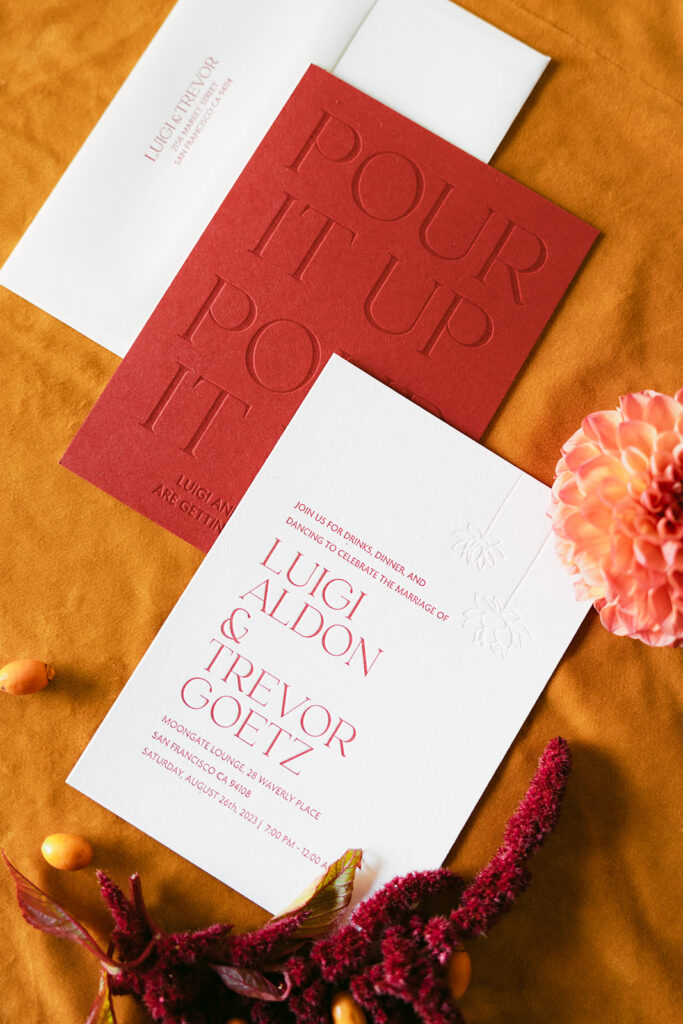 Wedding invitation suite of red and white invites with embossed design and orange background.