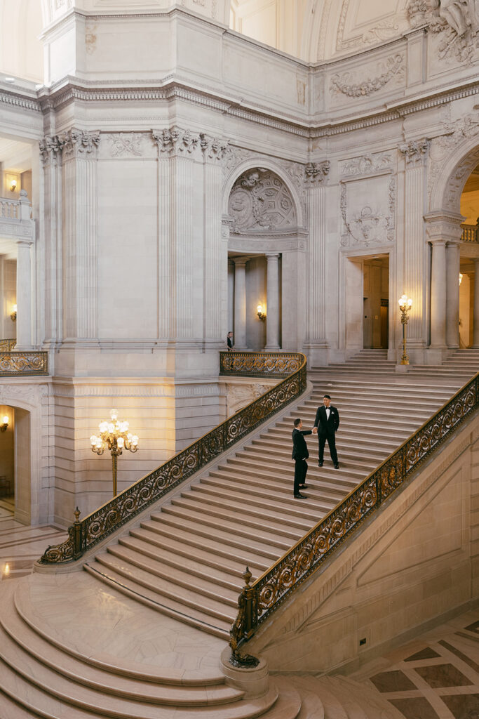Two grooms walking up the grand stairs of SF City Hall.