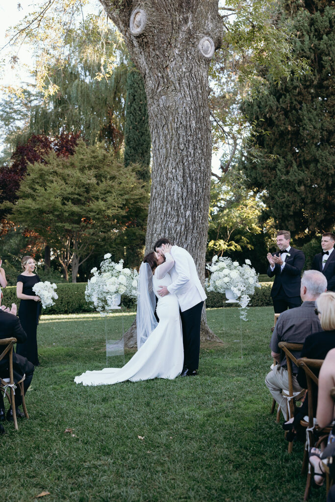 Bride and groom kissing under a large tree after saying I Do.