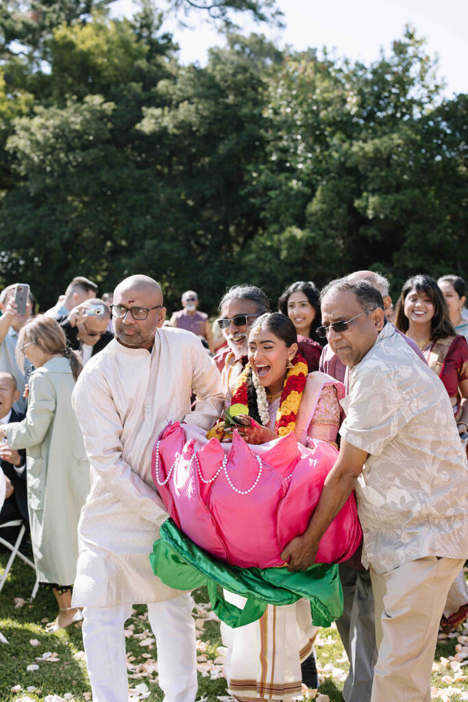 Bride being carried in pink floral doli by her male family members.