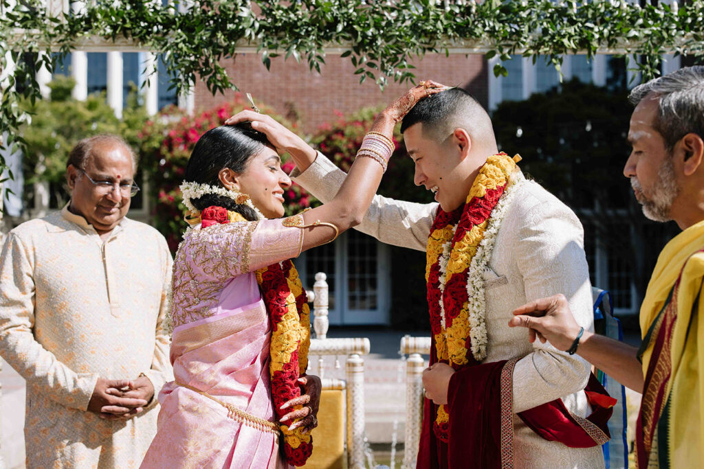 Bride and groom during traditional Indian wedding ceremony holding hands on each others heads.