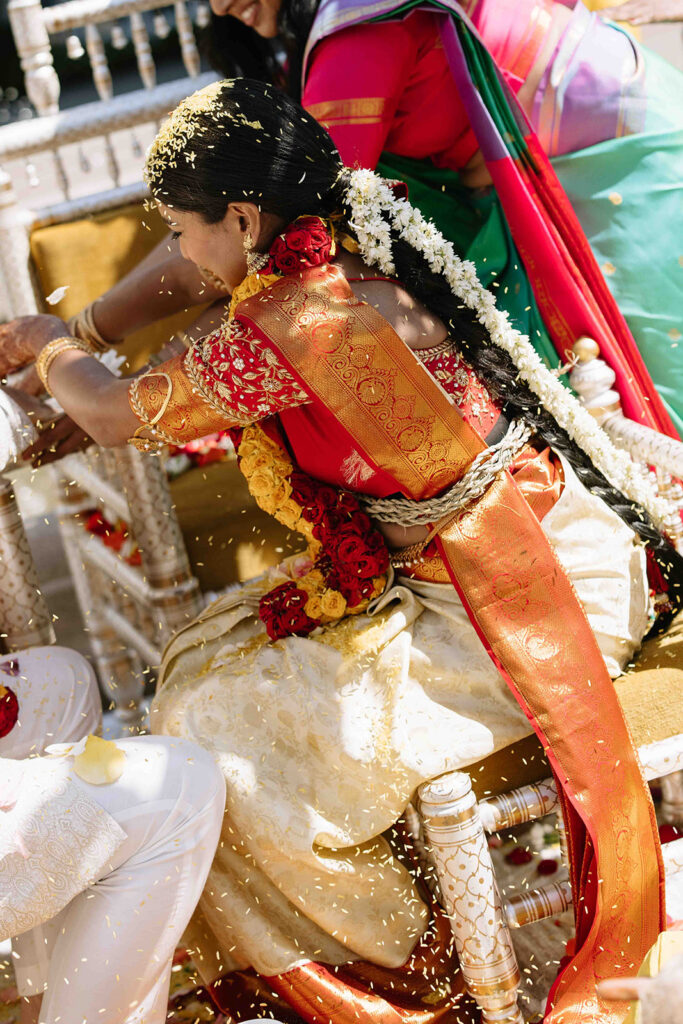 Bride covered in rice wearing a red and gold saree.