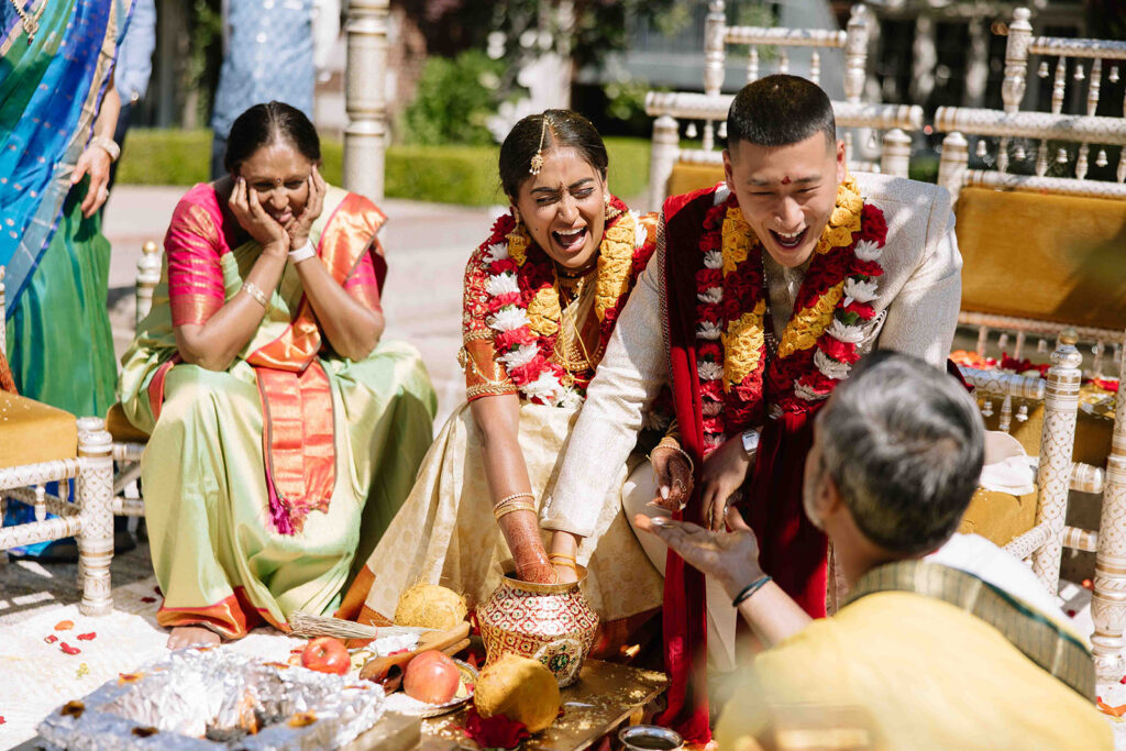 Bride and groom during traditional Indian wedding ceremony placing hands in vase.
