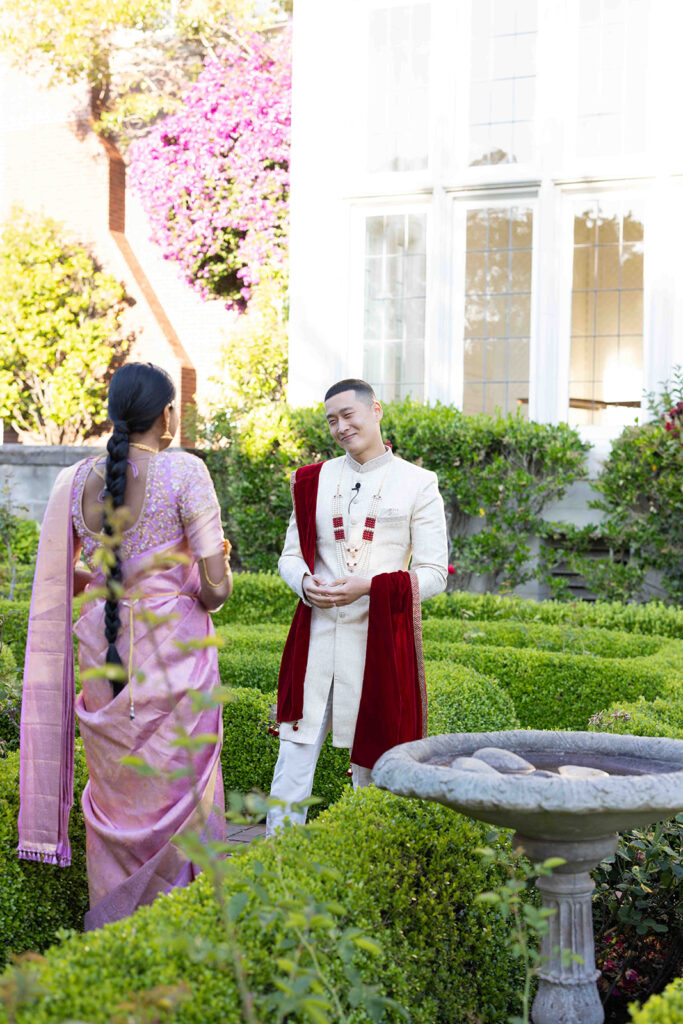 Groom smiling at bride as he sees her for the first time in her pink saree.