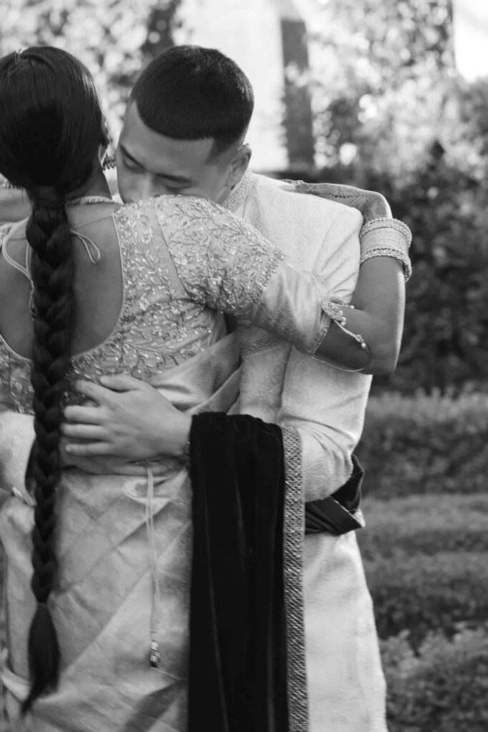 From behind the bride, the groom hugging bride and putting his head on her shoulder.