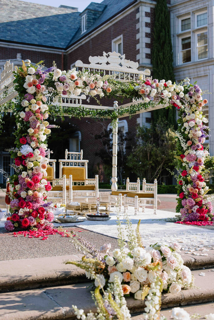 Indian mandap in white and hot pink florals with mustard yellow chairs.