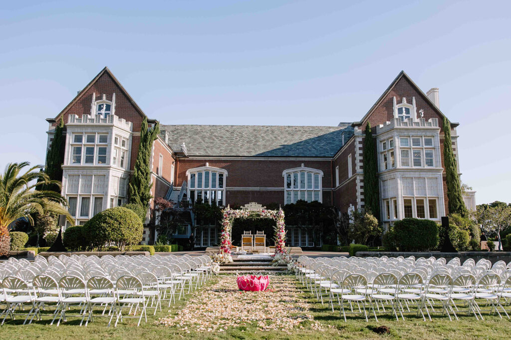 Indian mandap in white and hot pink florals with mustard yellow chairs in front of red brick mansion.