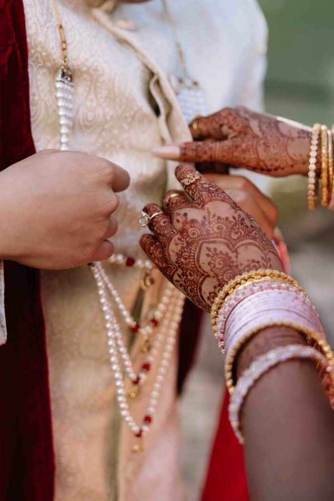 Bride adjusting the grooms sherwani. Details of her bridal henna and bangles.