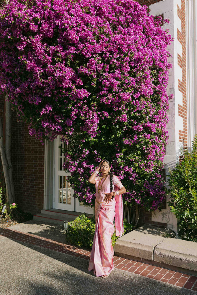 Bride in pink saree posing in front of bougainvillea.